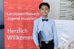 Lächelndes Kind vor dem Schriftzug Herzlich Willkommen zum Landeswettbewerb Jugend musiziert. Der Fotograf ist Uwe Hauth